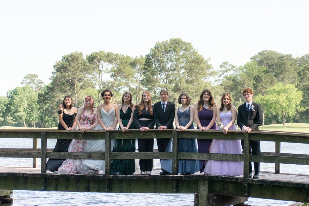 Formal group portrait on a wooden bridge with water and trees in the background.