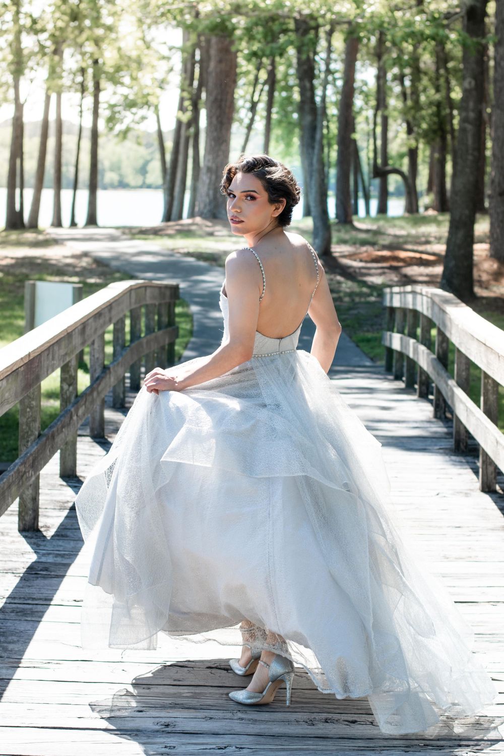 Bride in flowing white dress poses on wooden boardwalk surrounded by trees.