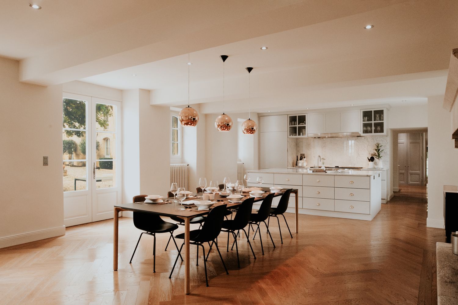 Modern open concept dining room and kitchen with copper pendant lights and hardwood floors.