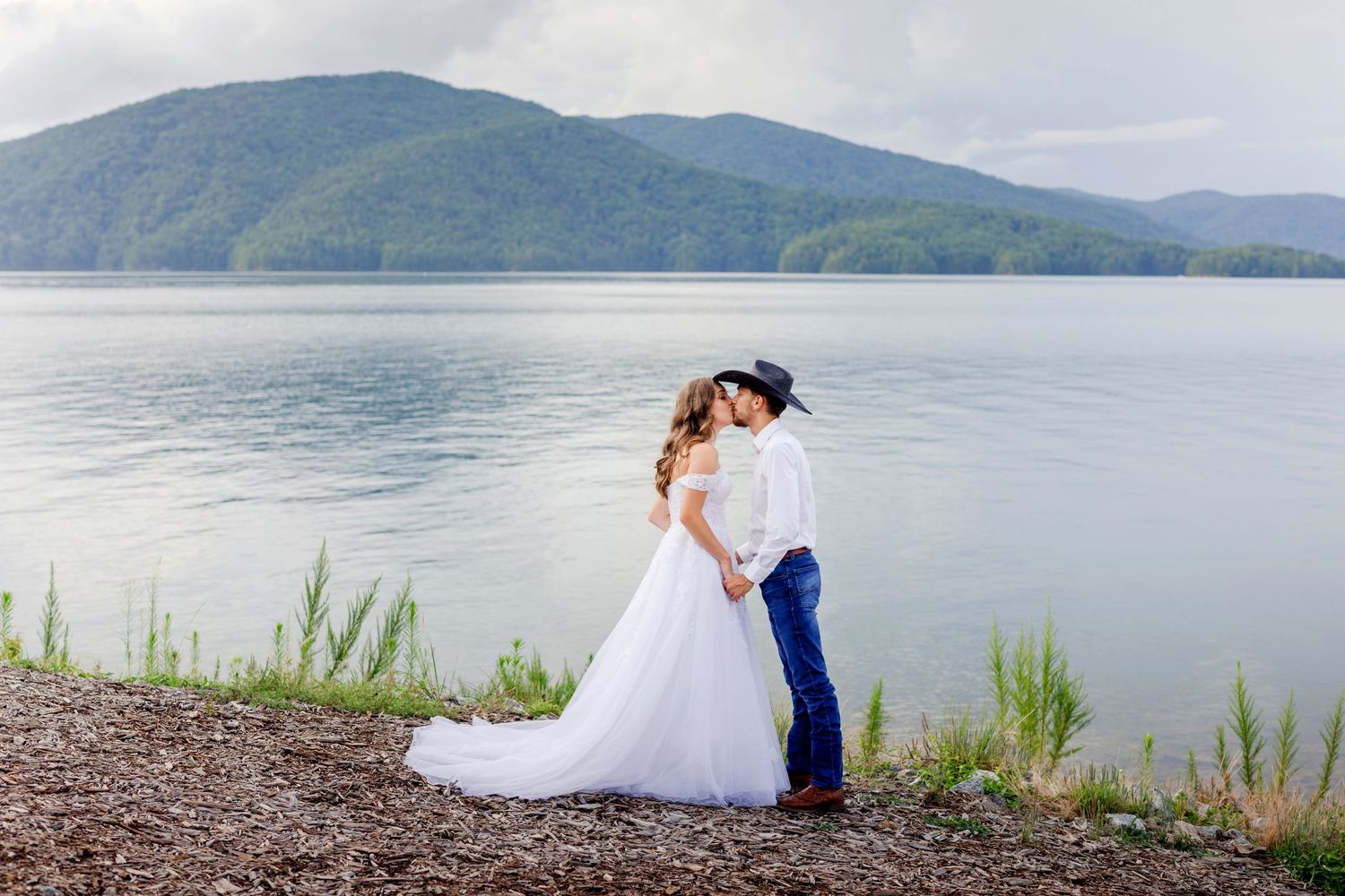Scenic mountain lake wedding portrait with couple embracing on shoreline.