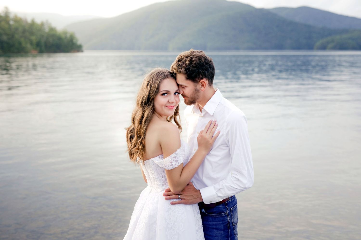 Romantic lakeside engagement photo with mountain landscape and serene water backdrop.