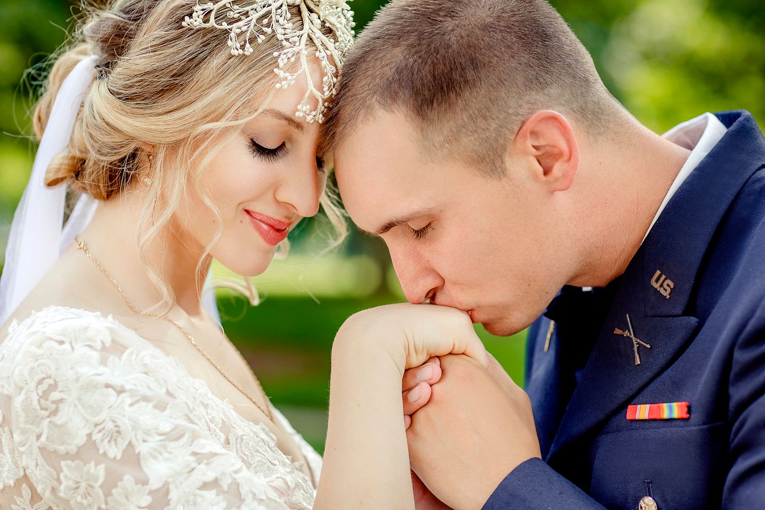 Intimate wedding moment captured outdoors with bride in lace and military groom in dress uniform.