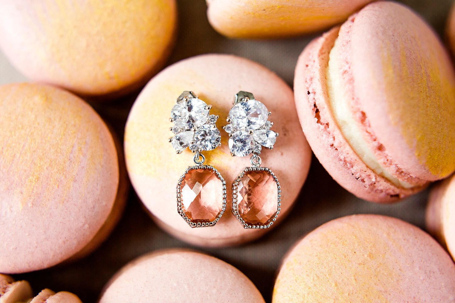 Elegant diamond and rose gold earrings displayed on pink macarons.
