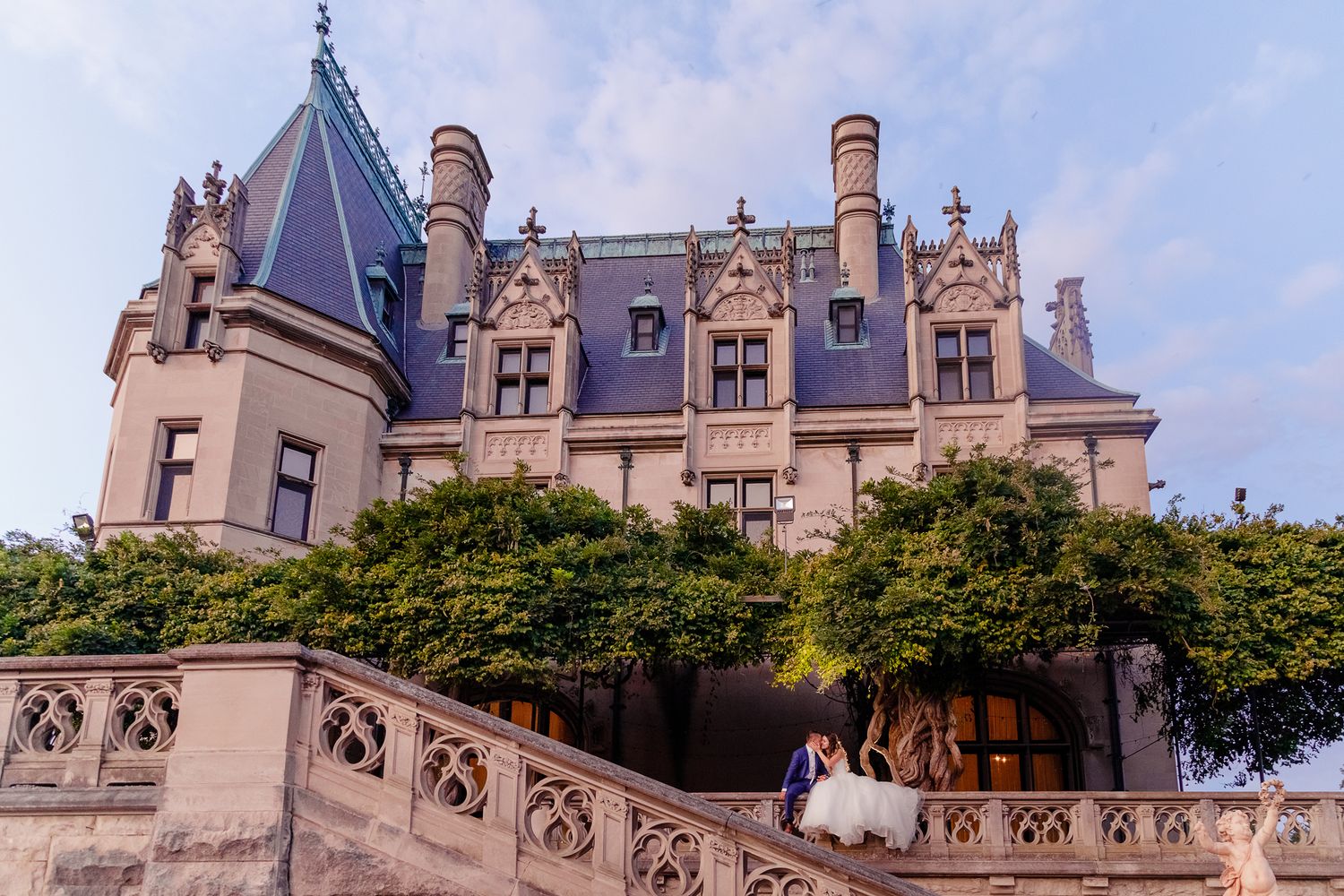 A grand stone castle with Gothic architecture serves as backdrop for a wedding photo.