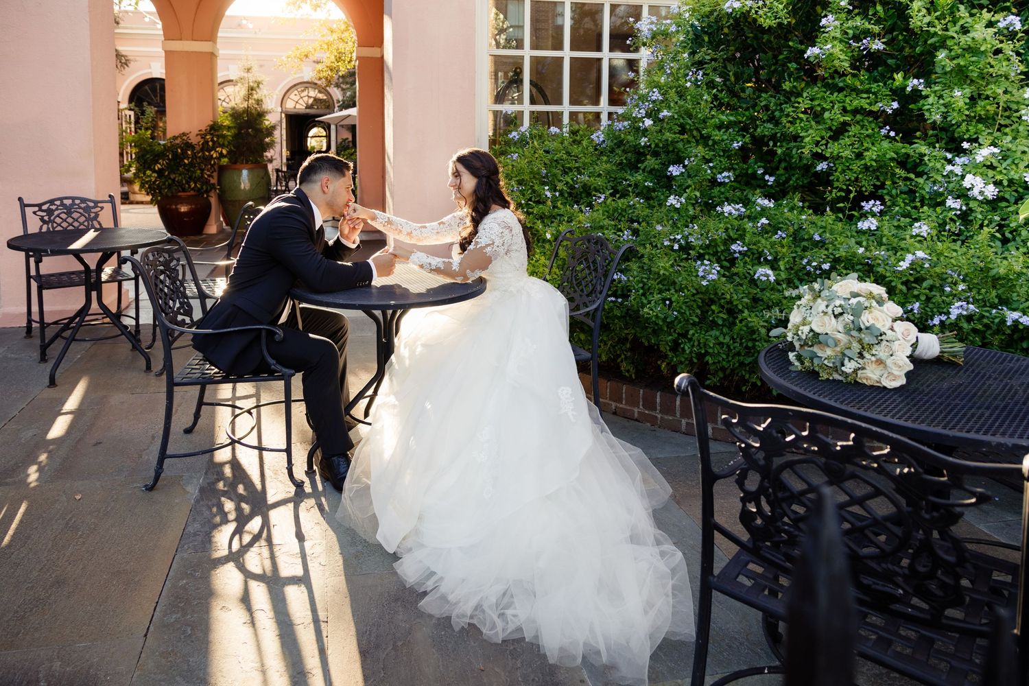 Wedding couple sitting at outdoor cafe table with elegant architectural details.