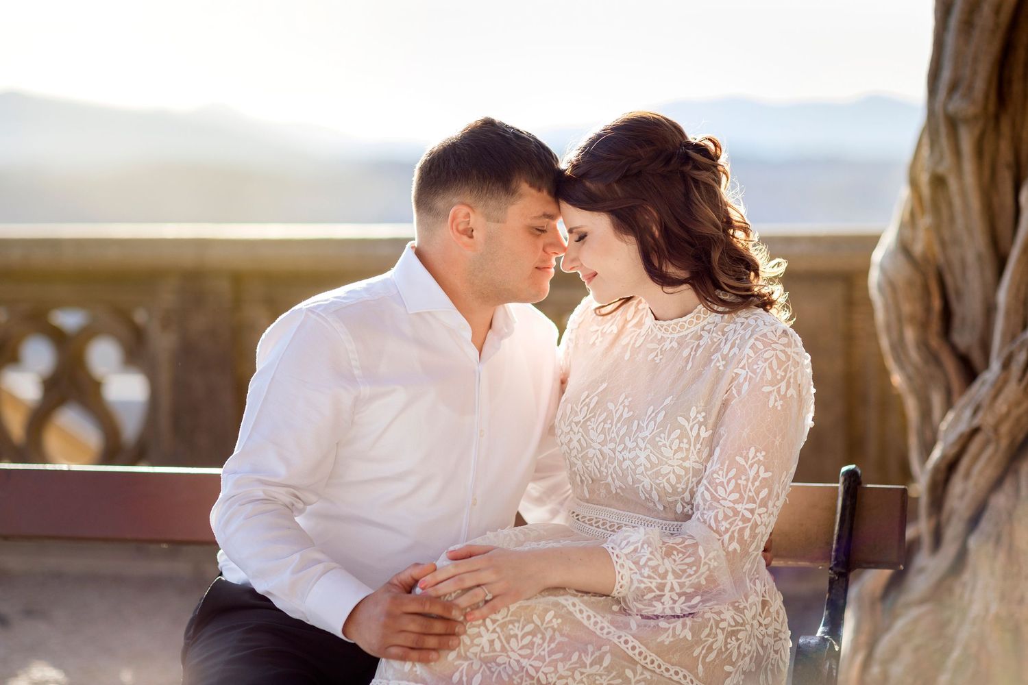 A couple shares an intimate moment on a stone balcony during sunset.