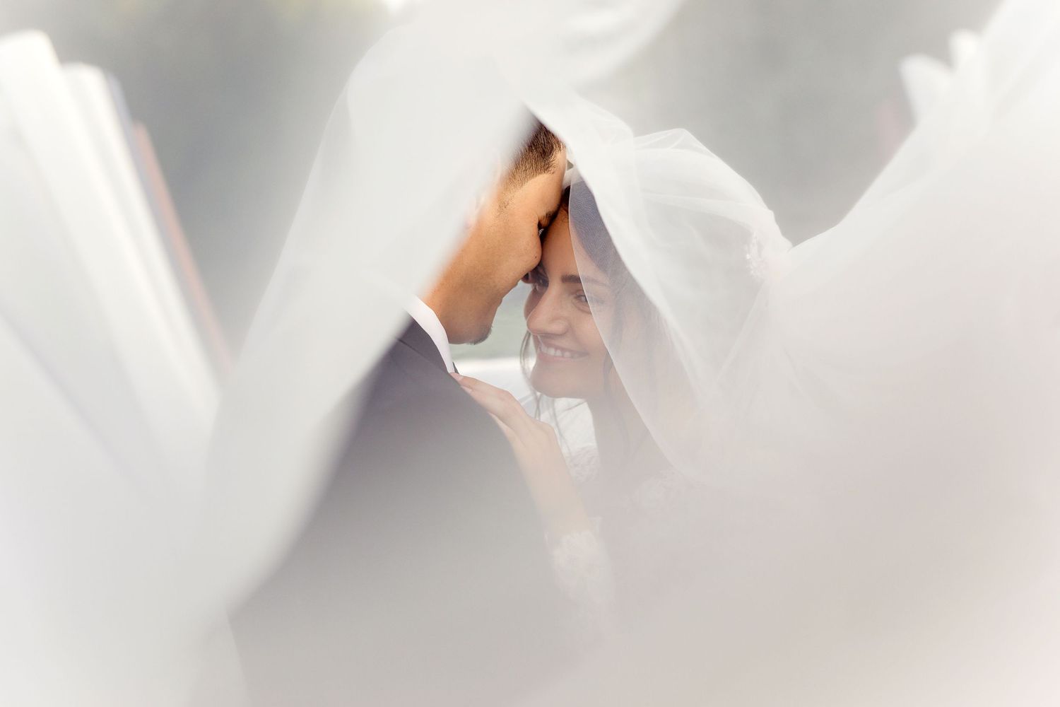 An ethereal wedding portrait through white veil creating soft romantic effect.