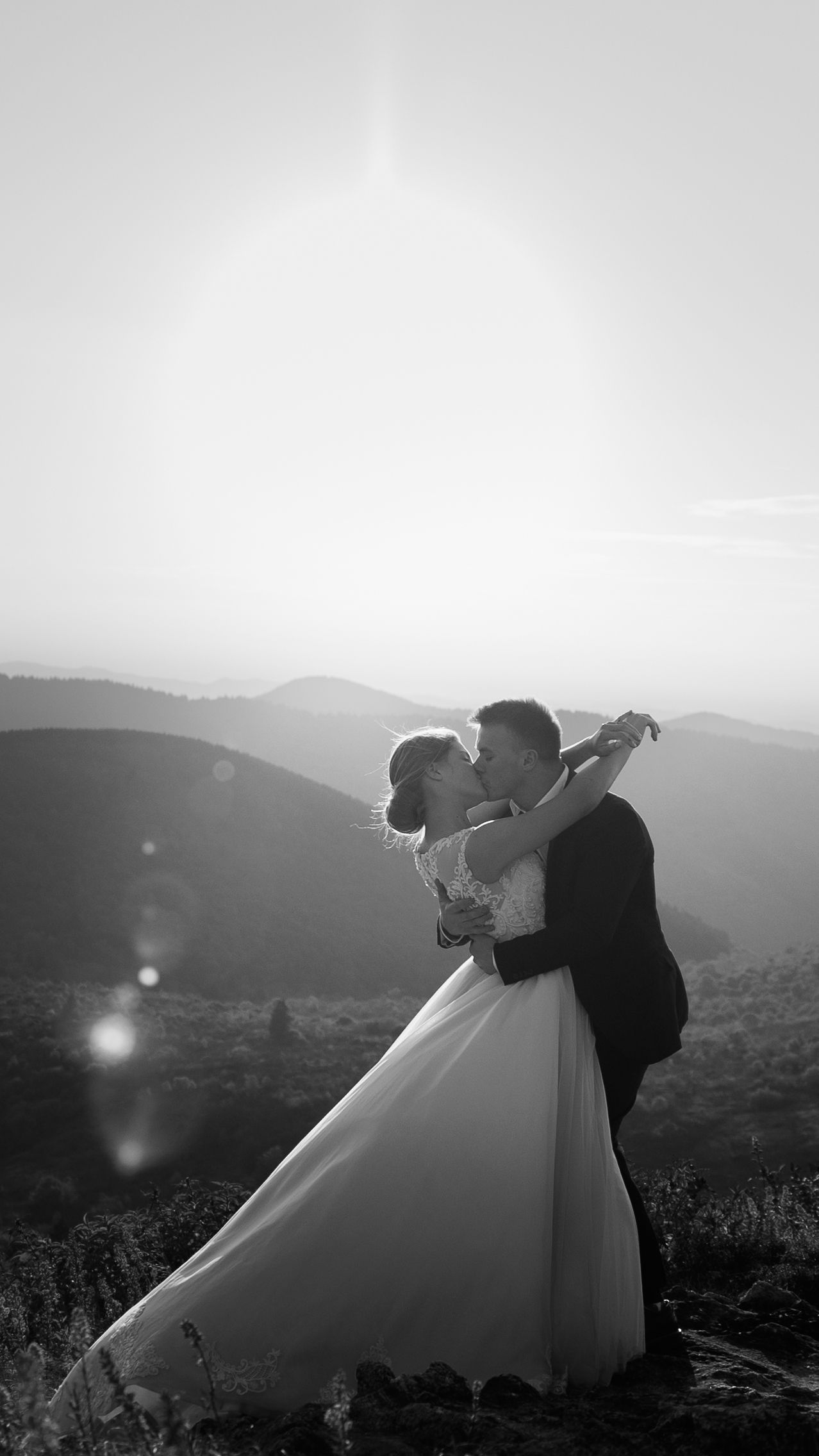 Black and white mountain wedding portrait silhouetted against scenic landscape.