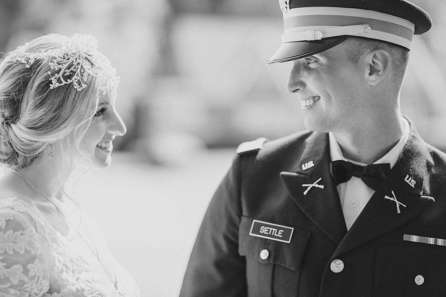 Black and white portrait of military groom and bride sharing joyful moment.