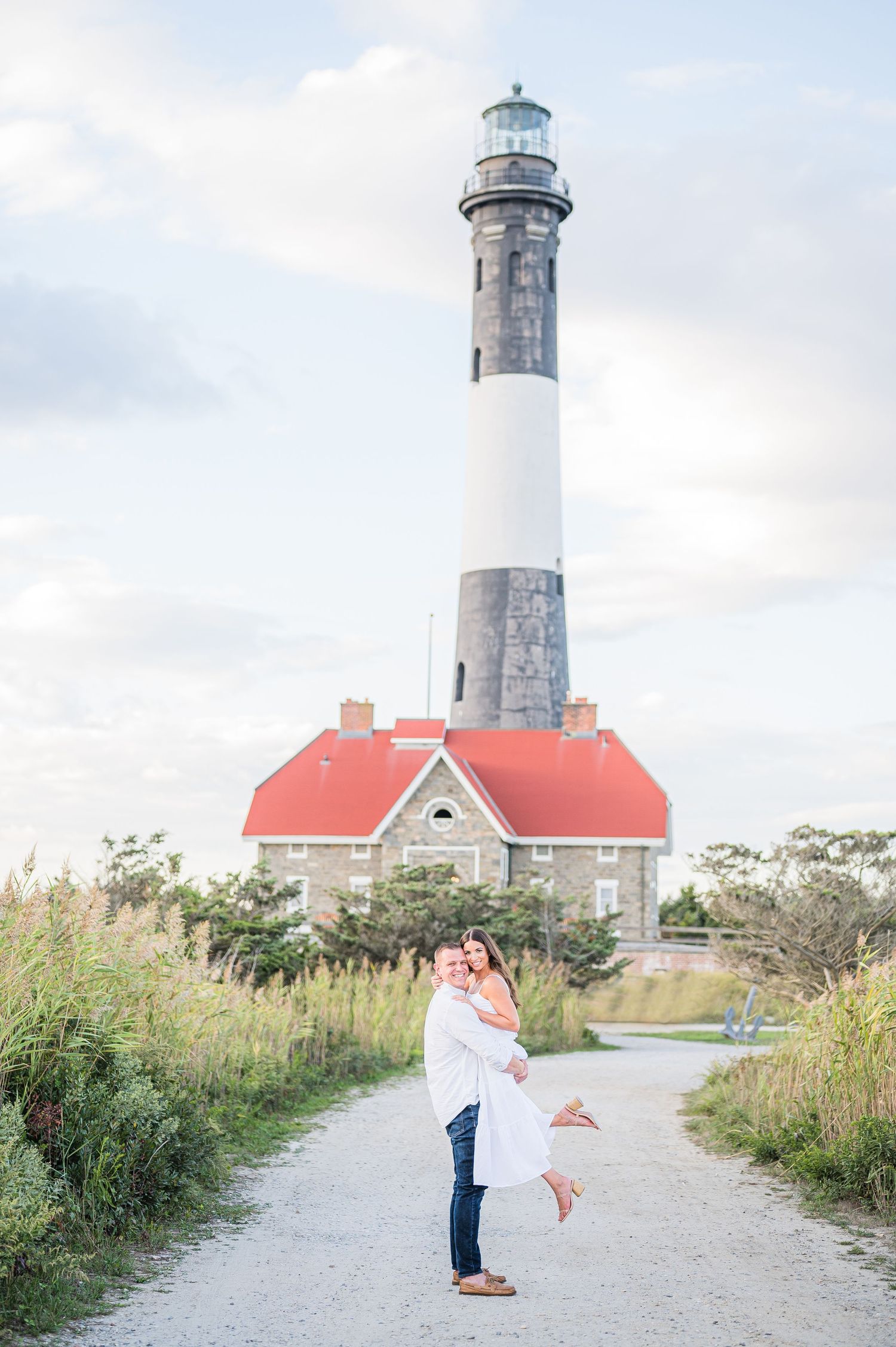 The groom lifts the bride happily with the Fire Island Lighthouse in the background.