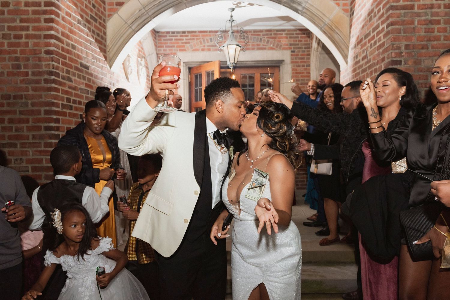 Bride and groom kissing in arched brick entryway with wedding guests surrounding them.