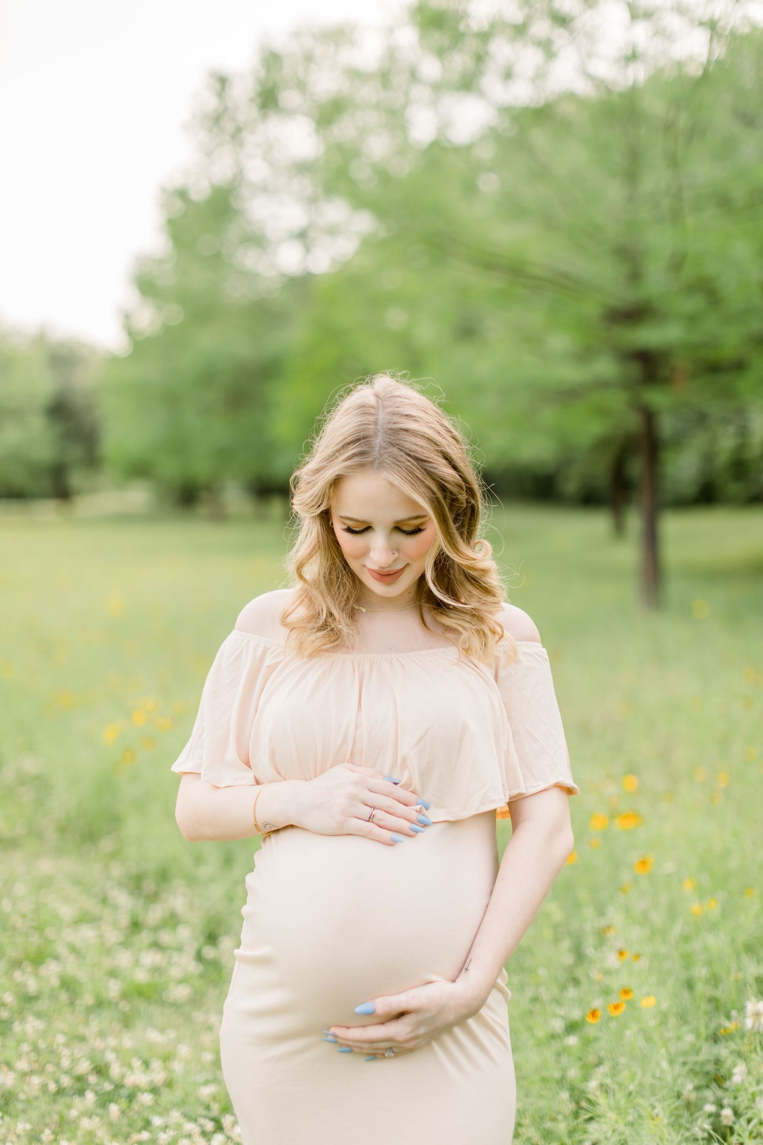 A soft, intimate maternity portrait in a blush gown amid spring greenery.