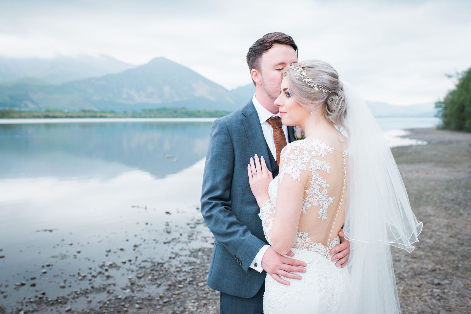 Couple share a kiss on the lake shore of Bassenthwaite with a view of the mountains behind