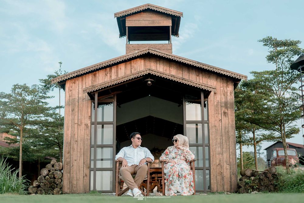 A couple poses together at a rustic wooden pavilion surrounded by greenery.