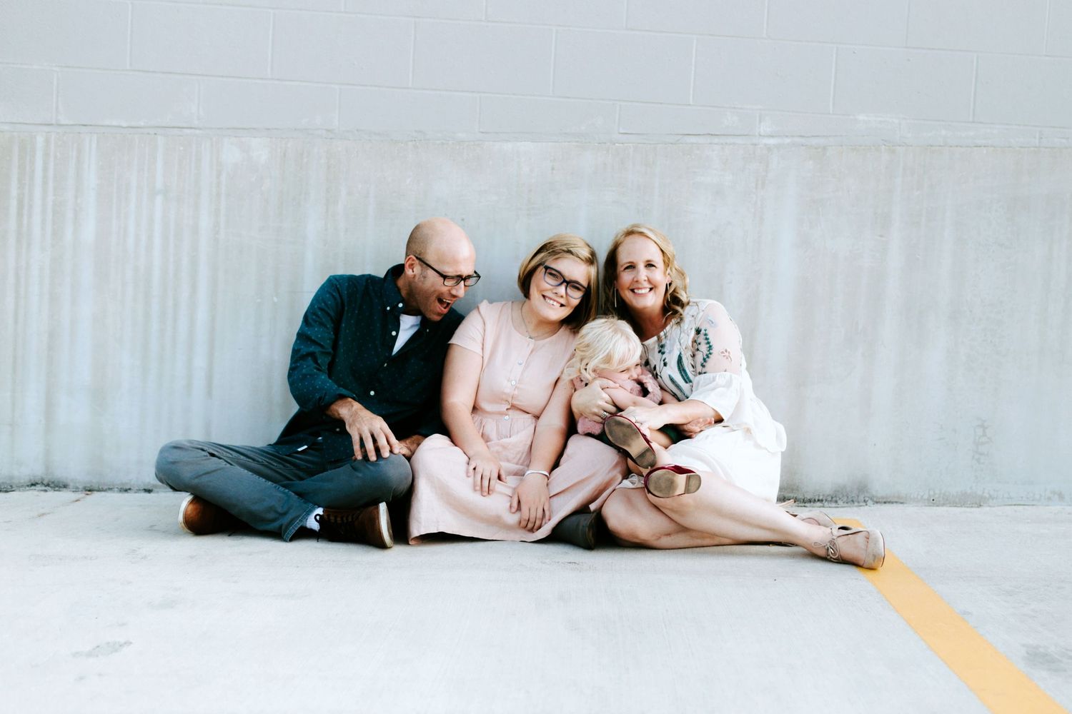 A loving family sitting together on the ground with their small dog while wearing casual comfortable clothing.