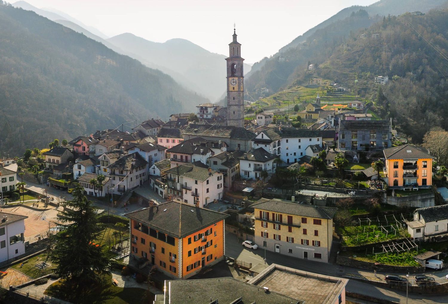 A mountain village nestled in a valley with a prominent church tower and colorful houses along the hillside.