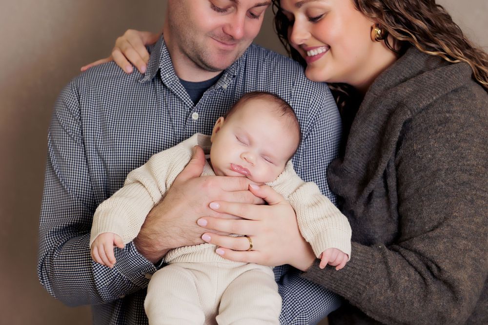 Family portrait showing intimate moment with sleeping baby cradled between parents.