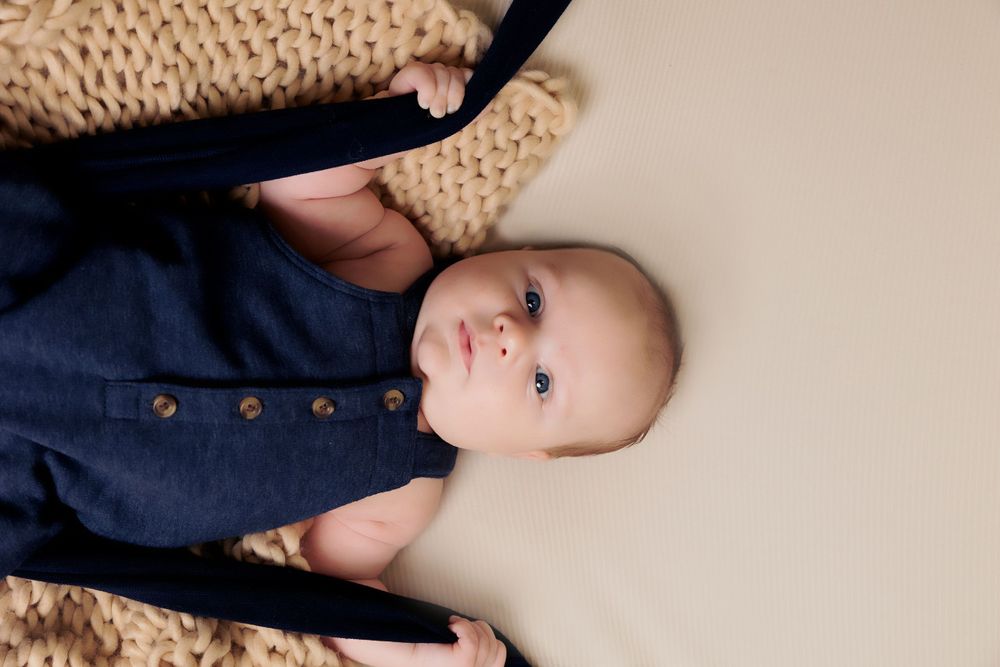 Baby wearing navy outfit laying on textured beige blanket during photo session.