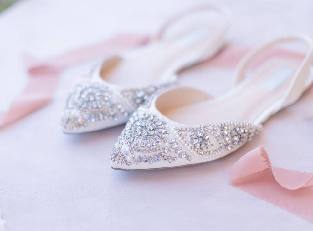 White beaded wedding shoes flat lay surrounded by pink satin ribbon.