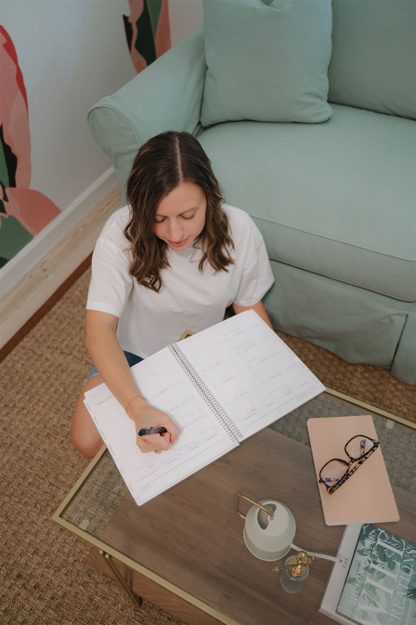 Writing in notebook on gold coffee table with eyeglasses and decorative items.