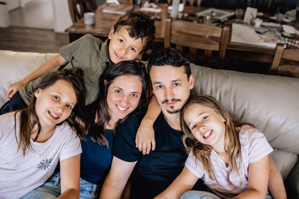 A family with three children looking at the camera, sitting on their couch for family photos