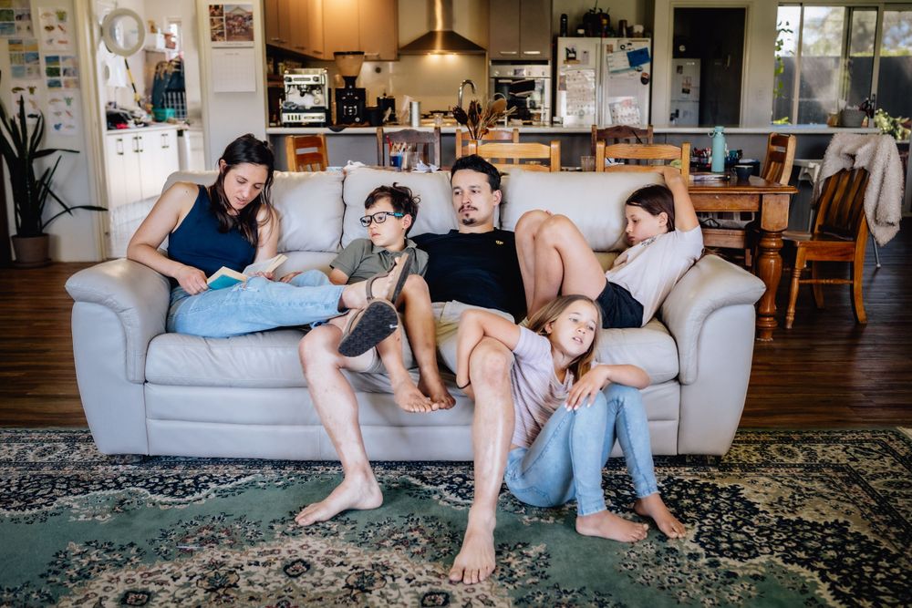 A family with three primary-aged children relaxed on a lounge in their home