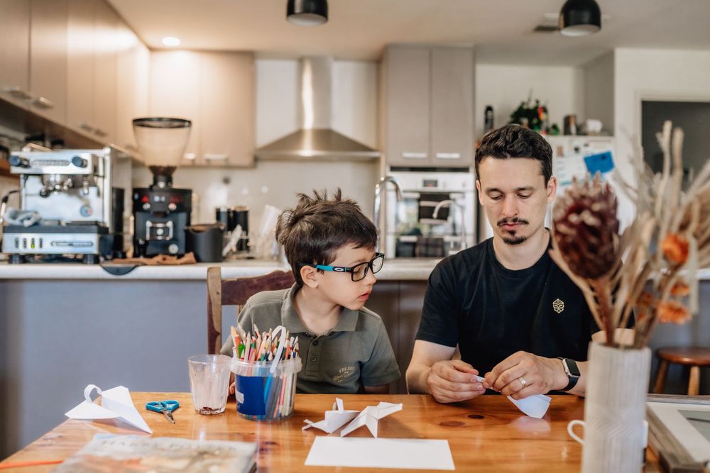 A dad and son making a paper aeroplane at their dining table in Perth