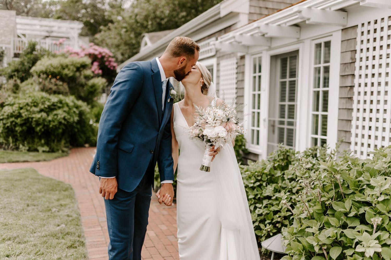 An intimate wedding portrait among blooming garden flowers against white latticed architecture.