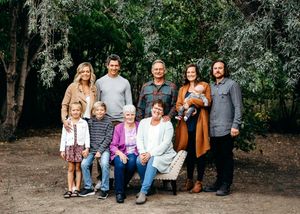 Multi-generational family portrait outdoors with trees, featuring adults and children smiling together.