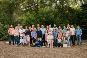 Large extended family group portrait outdoors on sandy ground with lush green trees behind.
