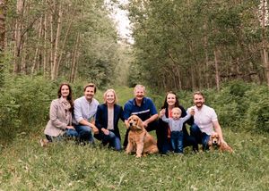 Family of seven with golden retriever dog posing together in green forest meadow.