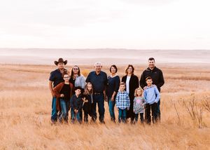 Multi-generational family portrait in golden prairie field wearing casual western-style clothing.