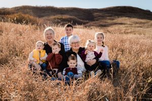 Two grandparents sit in golden prairie grass surrounded by seven young grandchildren during an autumn family photo session.