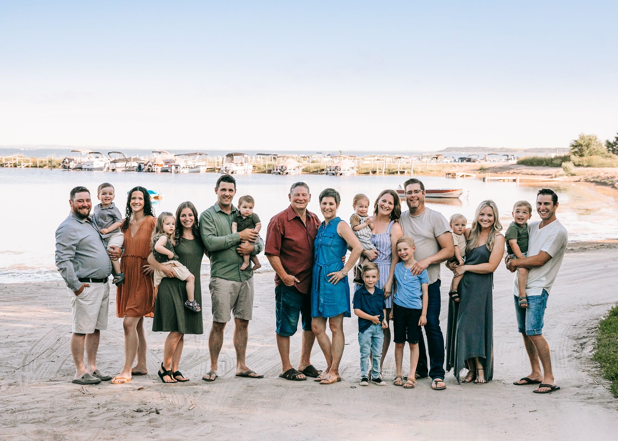 Large extended family posing together on a sunny lakeside beach during a summer gathering.