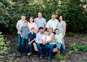 Extended family group portrait seated and standing outdoors surrounded by green garden foliage.