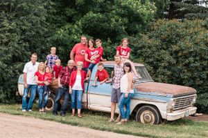 Large family in matching red shirts gathers around a rustic old blue pickup truck on a country dirt road.