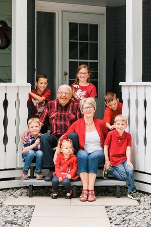 Grandparents in red sit on a porch steps surrounded by five grandchildren in coordinating red outfits.