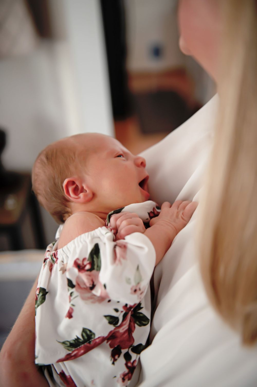 Newborn baby in floral outfit rests against caregiver in intimate moment.