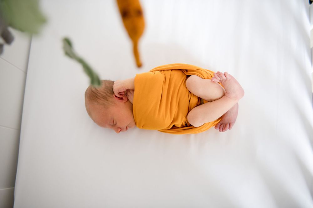 Close-up shot of hands cradling a newborn baby wearing bright yellow clothing.