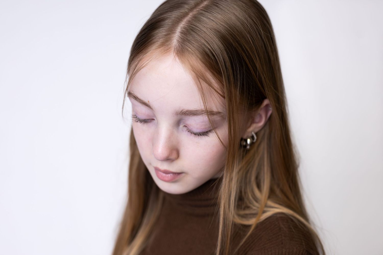 Close-up portrait of a young person with light hair looking down thoughtfully against white background.