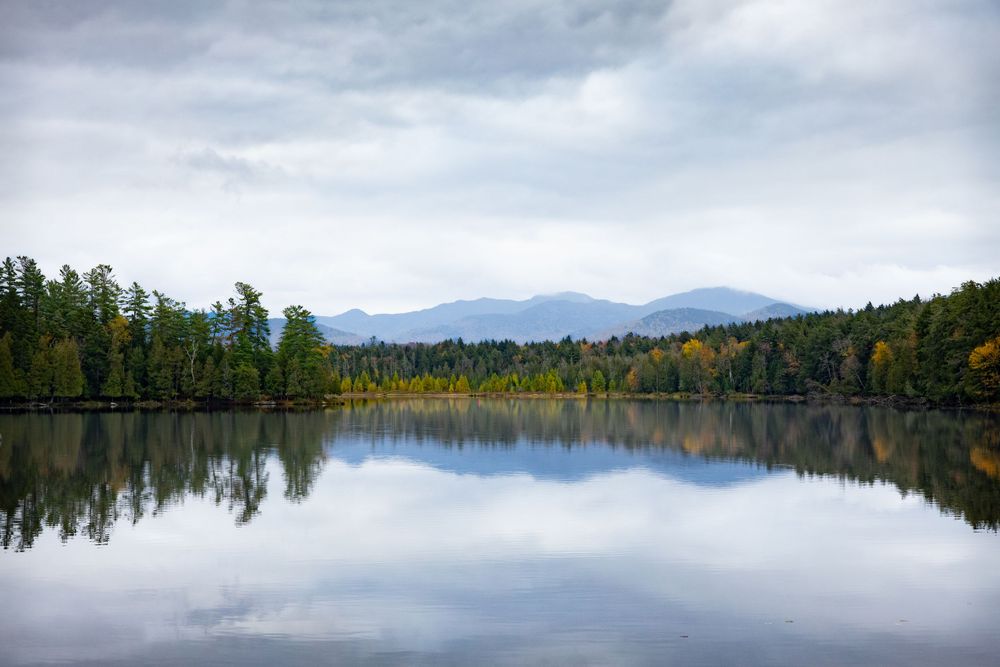 Serene mountain lake reflecting clouds and surrounding forest in perfect symmetry.
