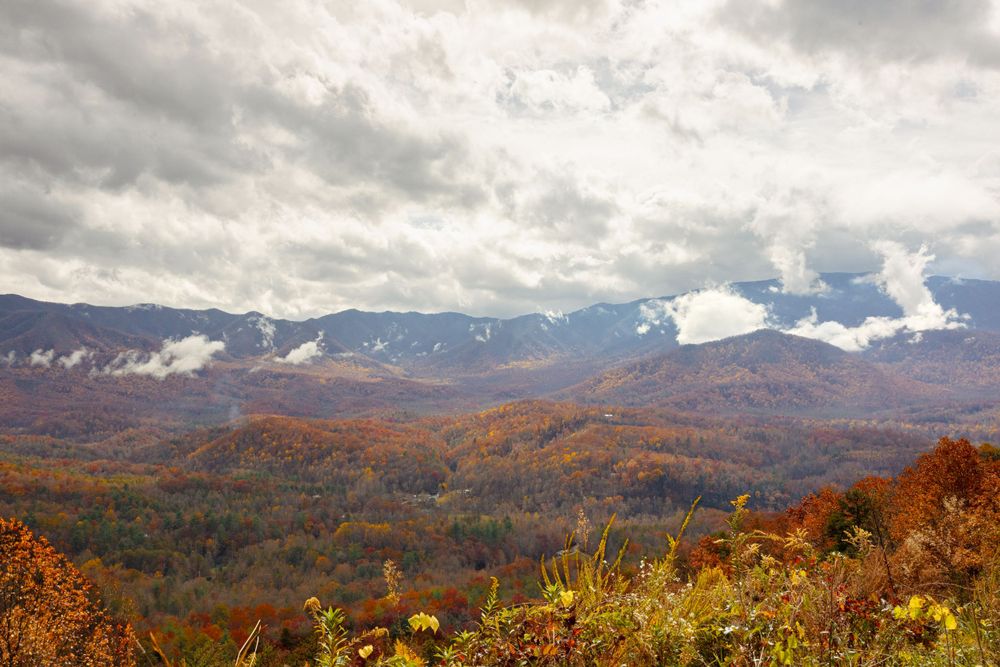 Dramatic mountain landscape with autumn foliage and cloudy skies over rolling hills.
