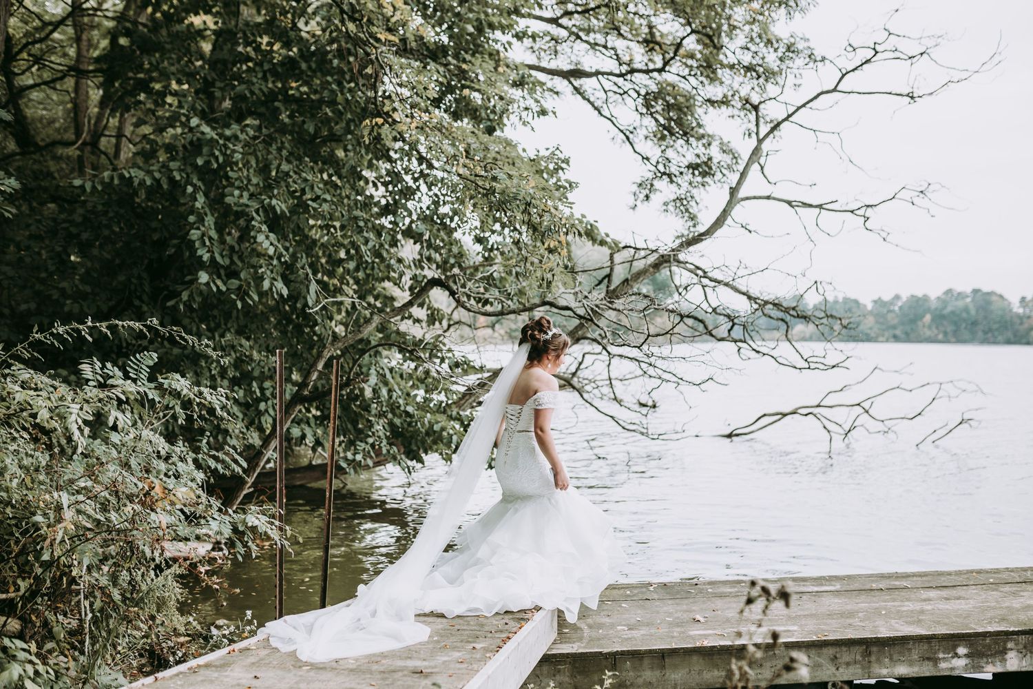 A flowing white wedding dress captured on a dock by a serene lake.