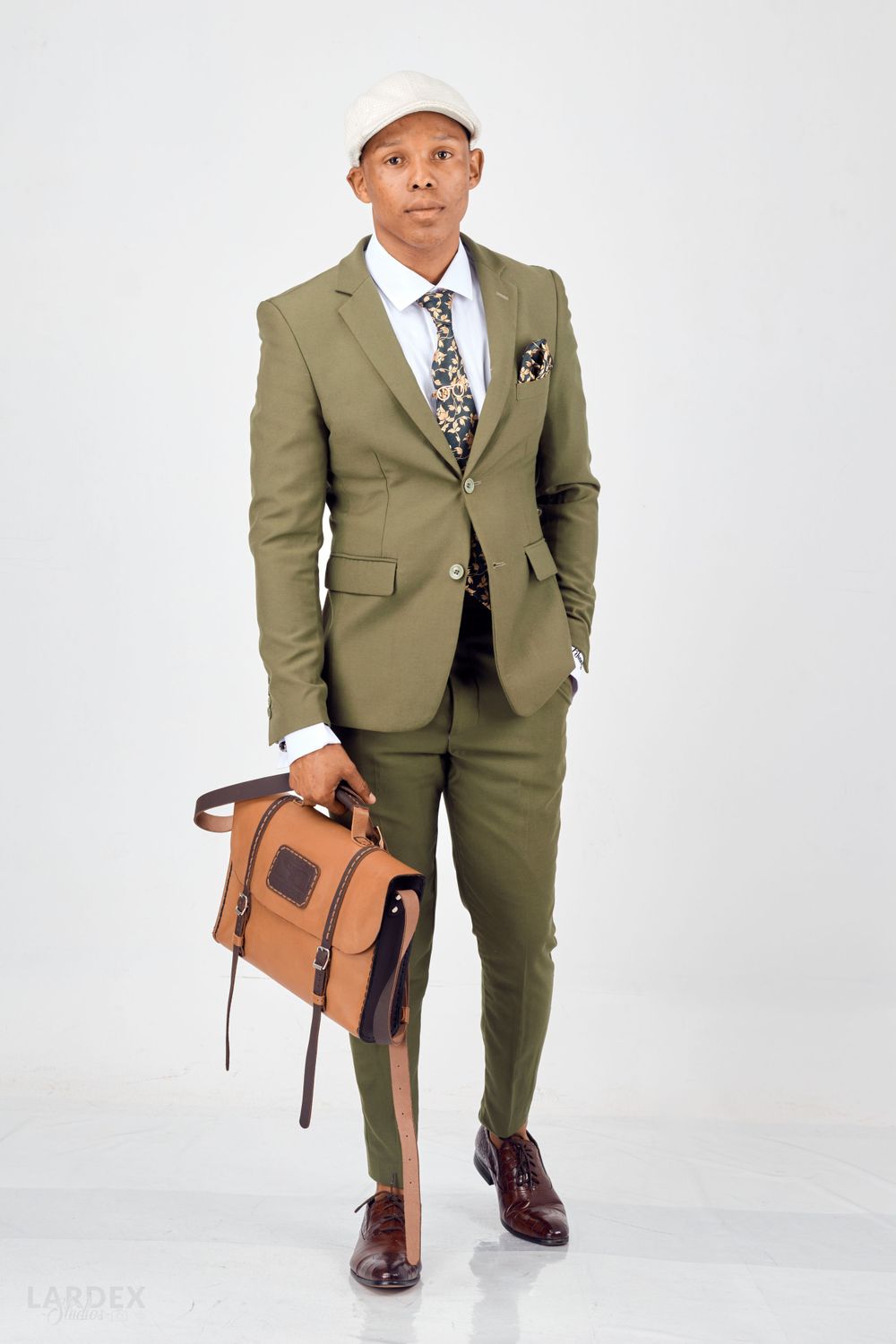 Professional fashion shot of stylish olive suit paired with brown leather bag against white background.