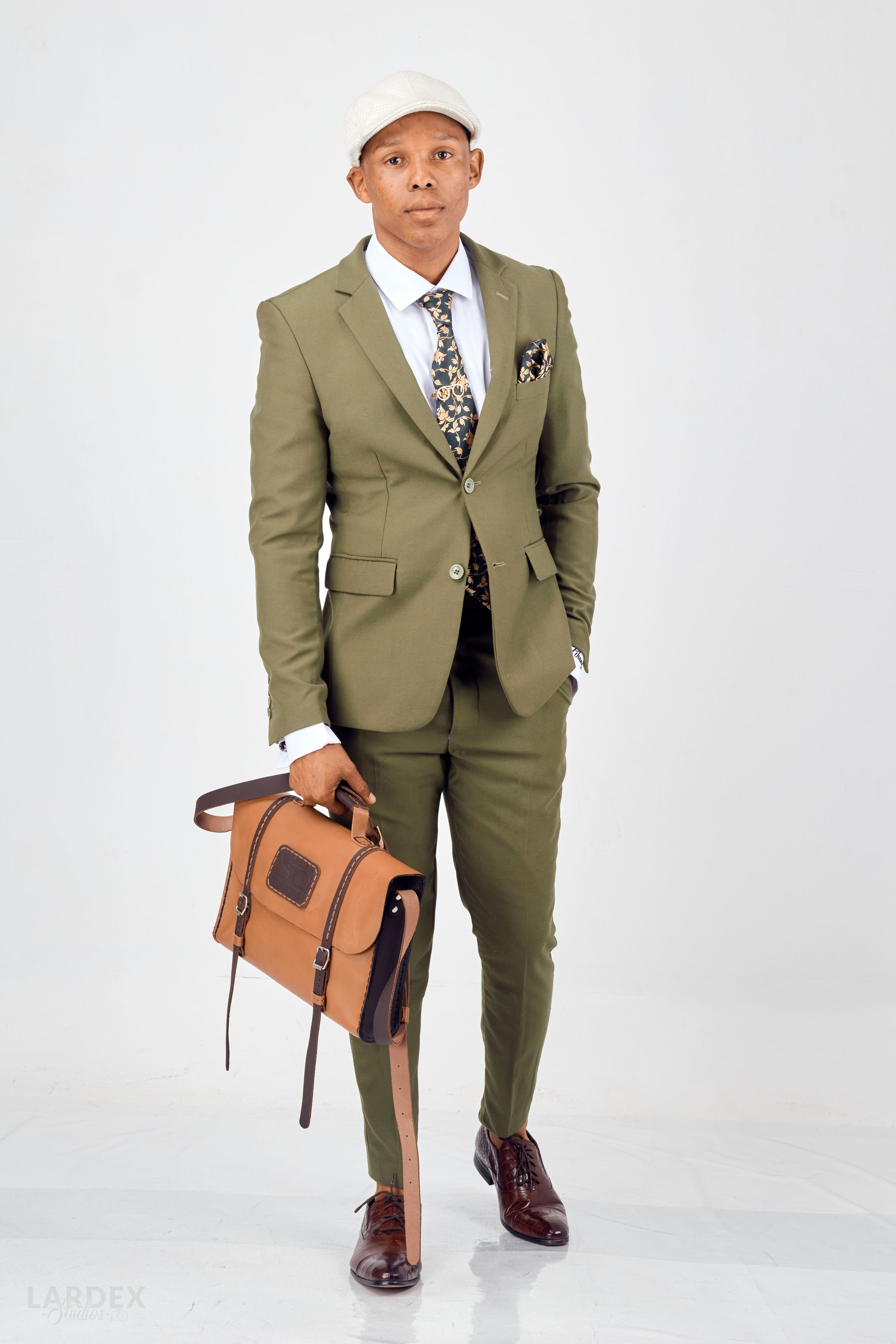 Professional fashion shot of stylish olive suit paired with brown leather bag against white background.