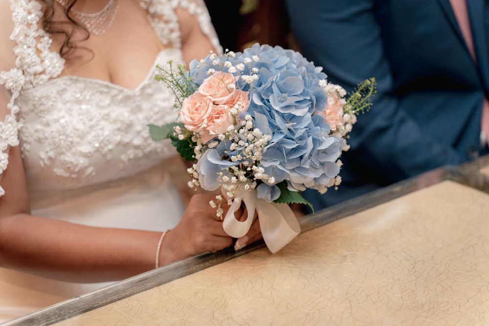 Close-up of wedding bouquet featuring blue hydrangeas and peach roses tied with a beige ribbon.