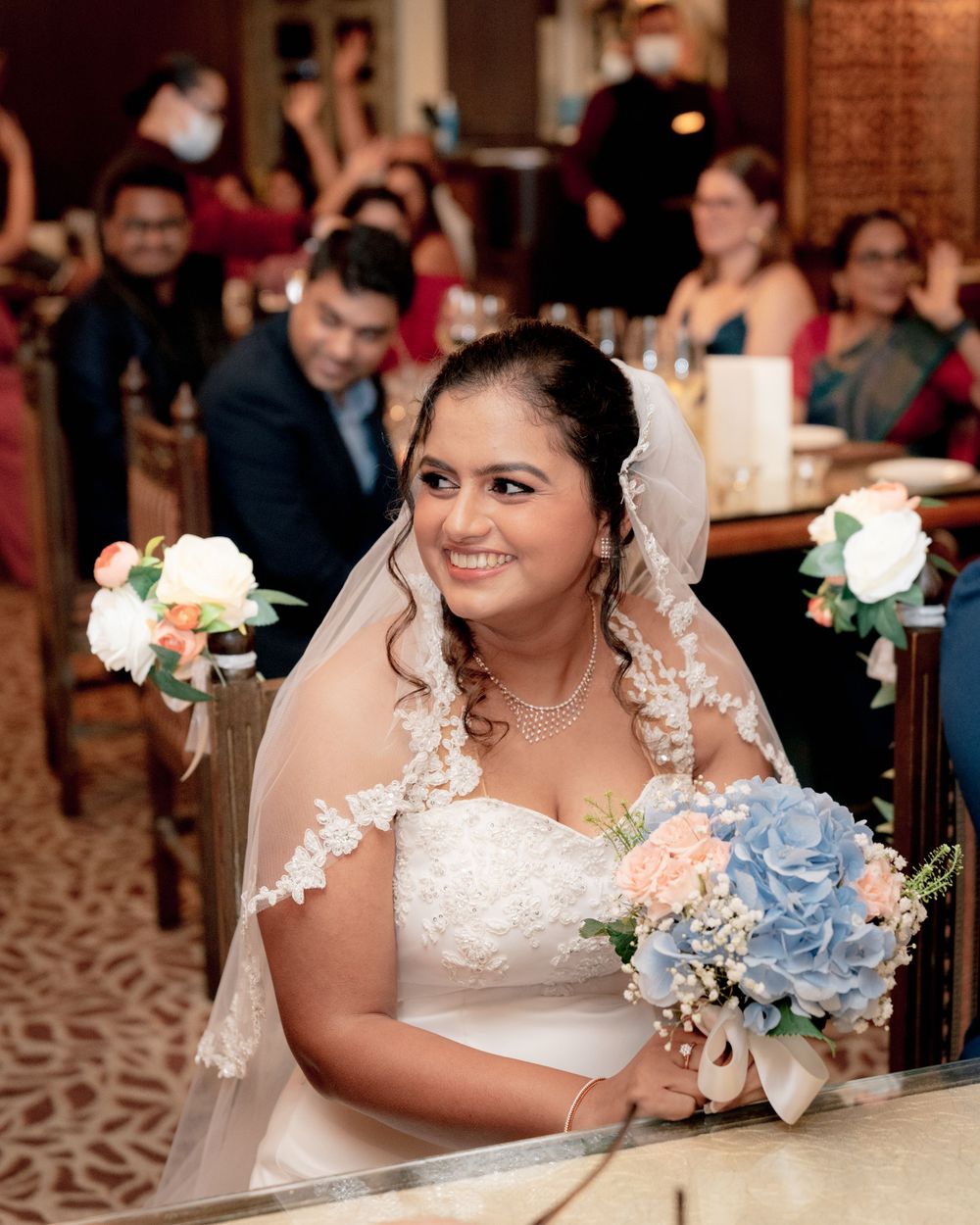Bride holds bouquet of blue hydrangeas while smiling during wedding reception.