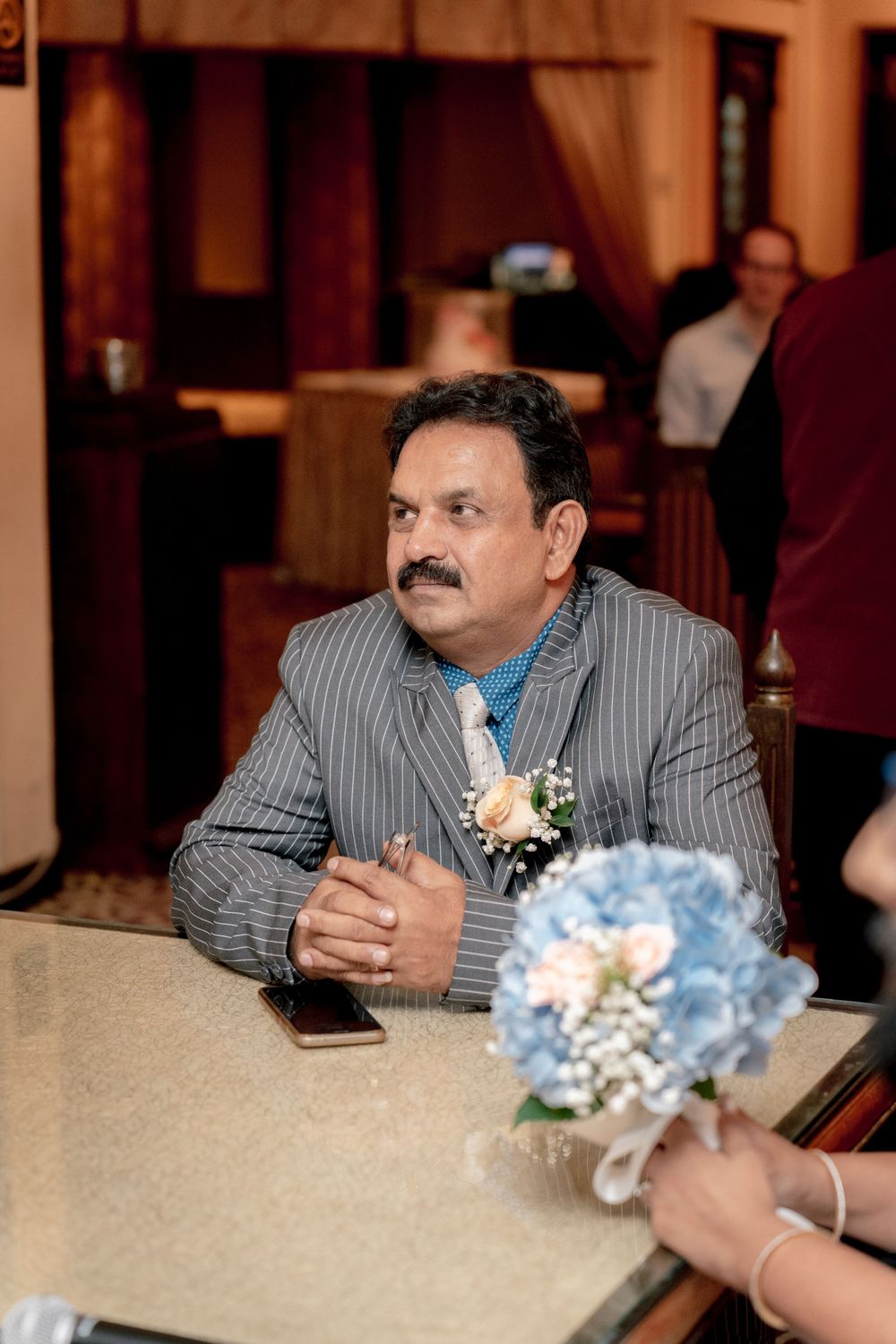 Wedding guest in a grey suit sitting at reception table with blue hydrangea centerpiece.