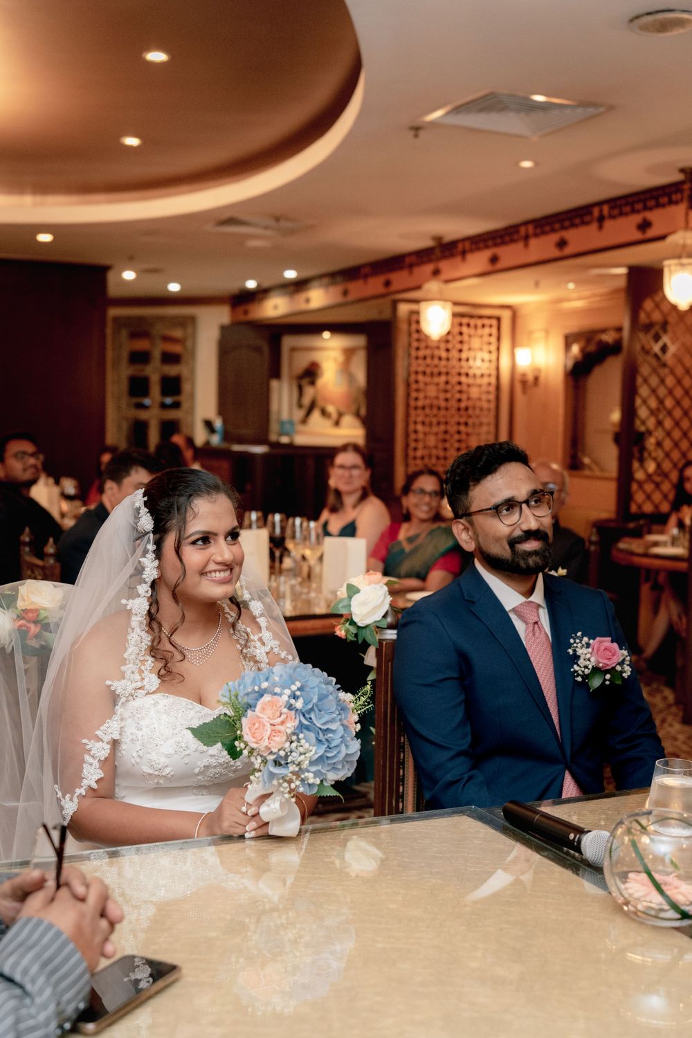 Newlyweds seated at reception table with blue and peach floral bouquet arrangements.