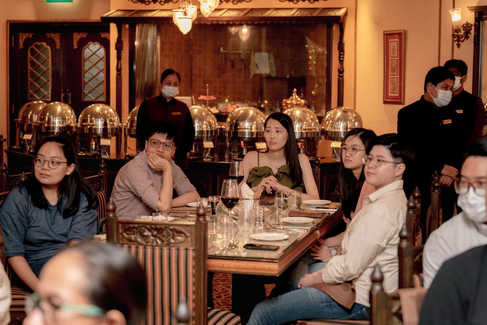 Wedding guests seated at elegant dining tables in a restaurant with crystal chandeliers overhead.